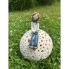 Ceramiczna figurka kobiety siedzącej na ażurowej kuli